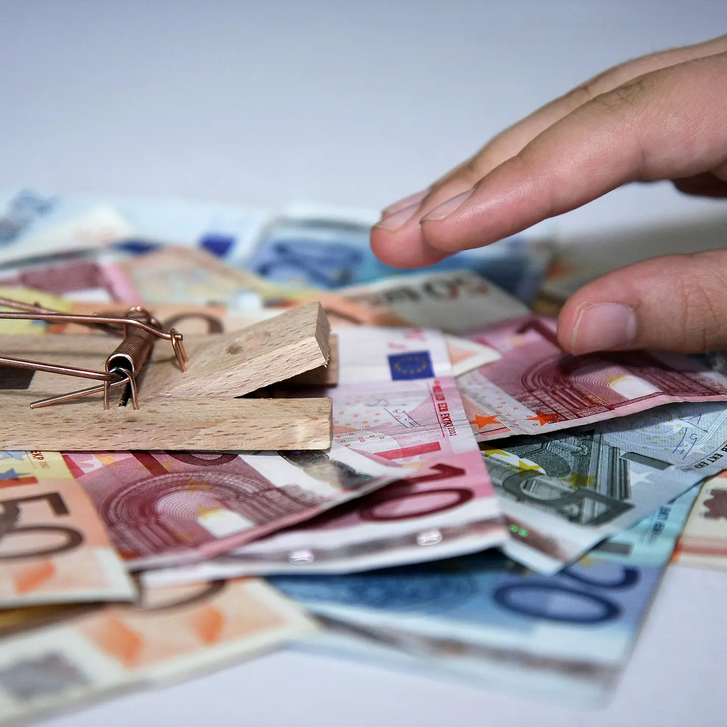 Hand greift nach Geldscheine die mit Mausefalle auf einem Tisch liegen