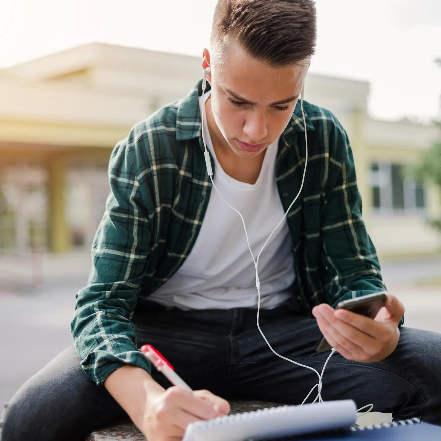 Ein junger Mann sitzt mit Laptop draußen auf einem Hochschulcampus. 