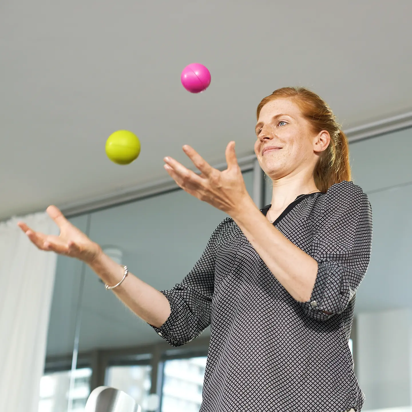 Eine Frau steht im Büro und jongliert mit zwei Bällen.