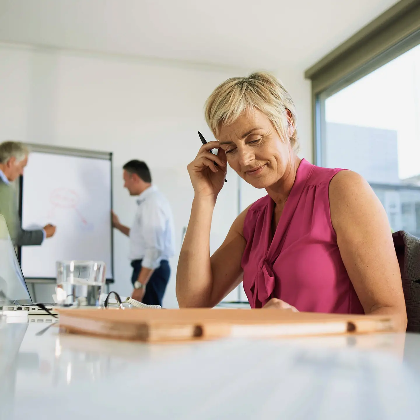Blonde Frau sitzt grübelnd über einer Akte im Büro.