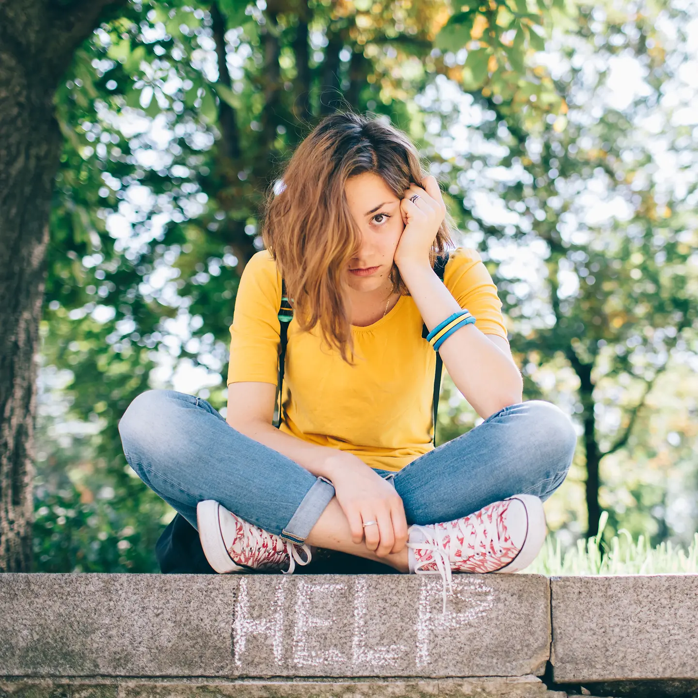 Nachdenkliche junge Frau sitzt auf einer Mauer, auf der das Wort Hilfe in englischer Sprache steht.