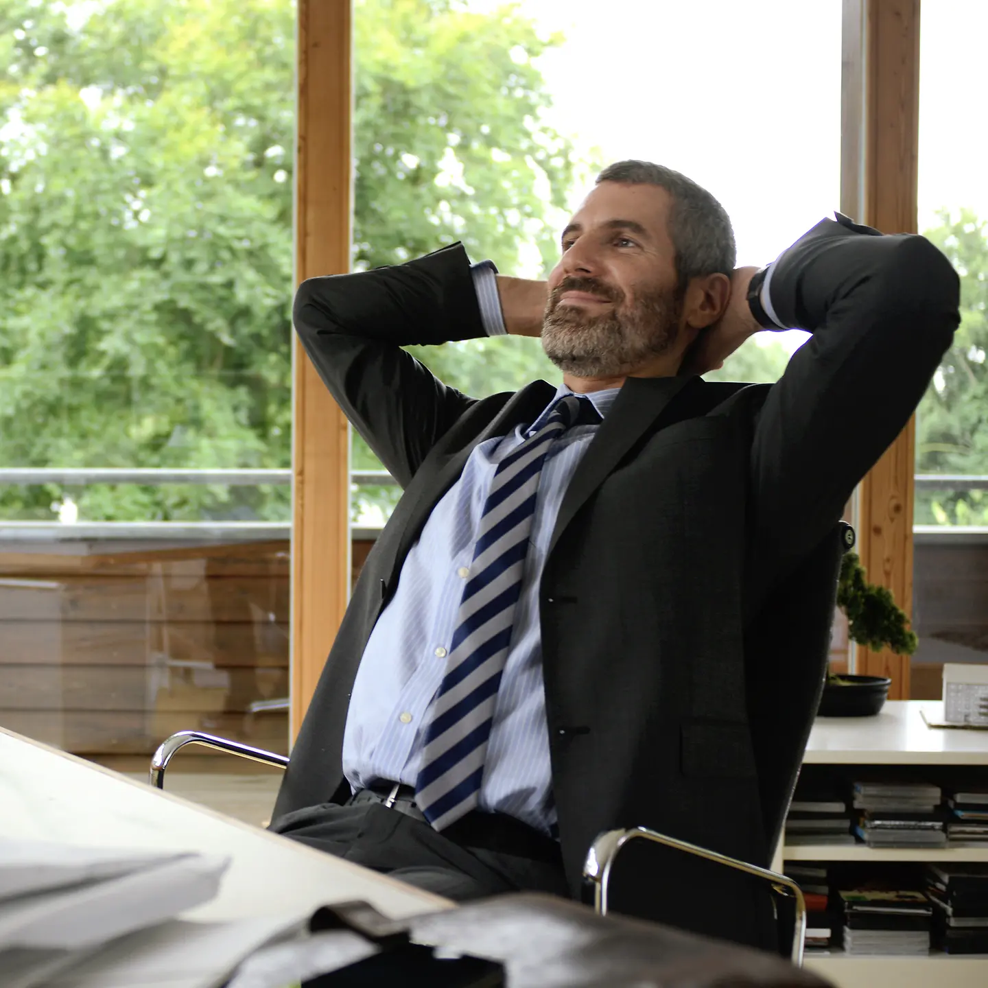 Ein entspannt ausschauender Mann sitzt am Schreibtisch und hat die Hände hinter dem Kopf verschränkt.