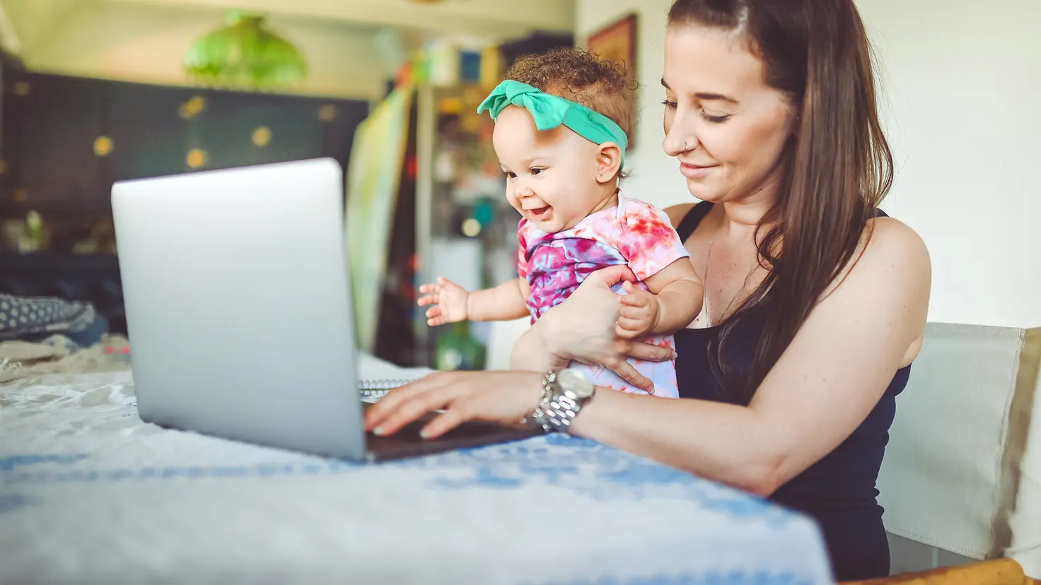 Eine Frau hält ihr Baby auf dem Arm, beide schauen in einen Laptop