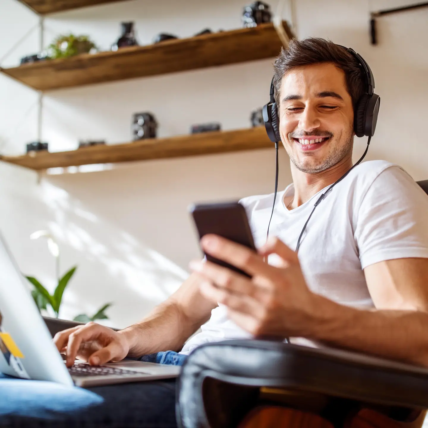 A young man sits at the laptop and listens to music with headphones.