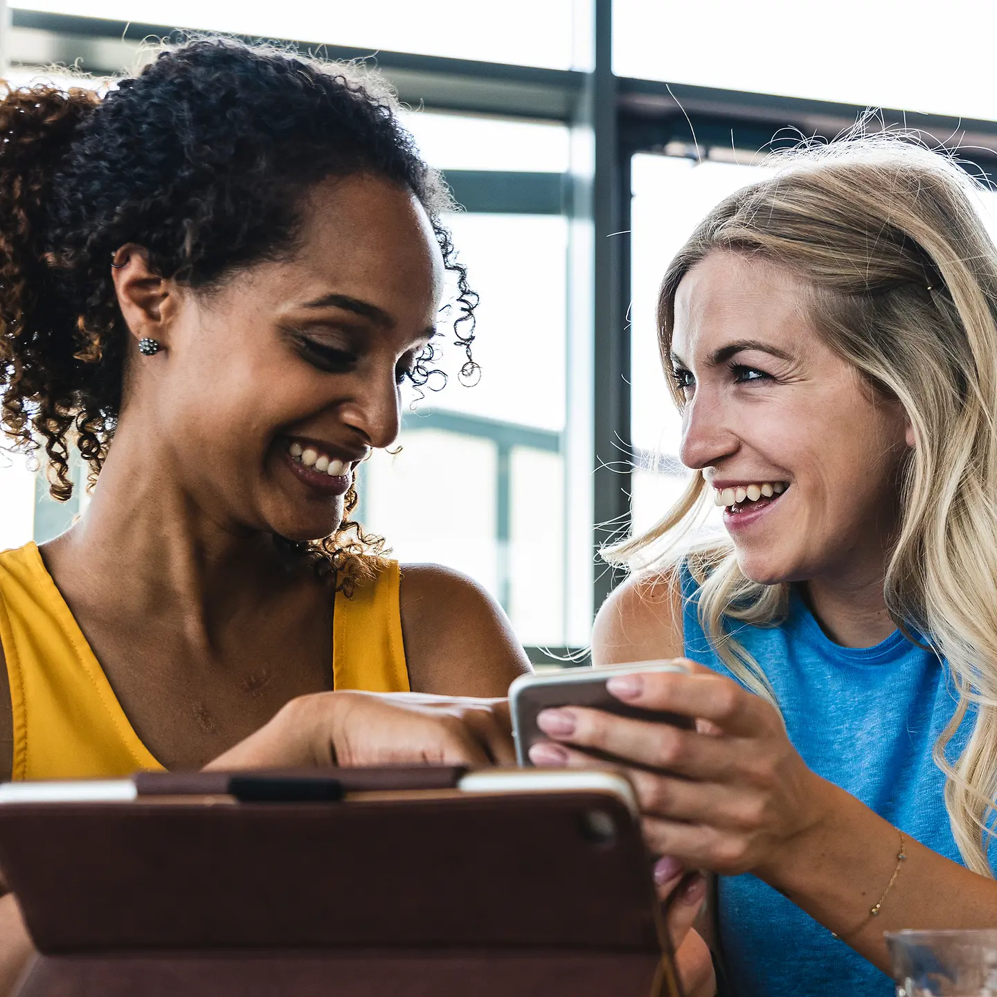 Two young women with digital devices laughing together