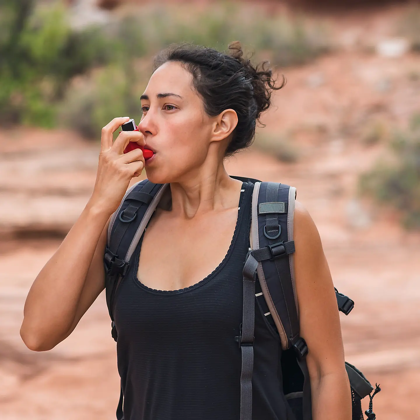 Eine Frau mit Rucksack benutzt während einer Wanderung ihr Asthmaspray.