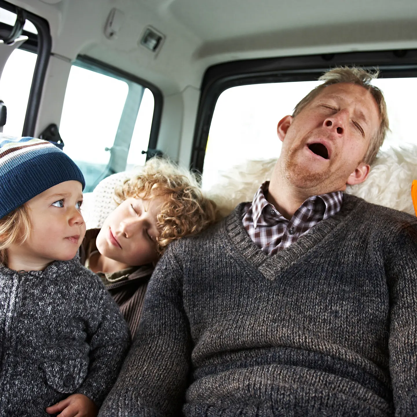 Ein Vater sitzt mit drei Kindern auf der Rückbank eines Autos und schläft