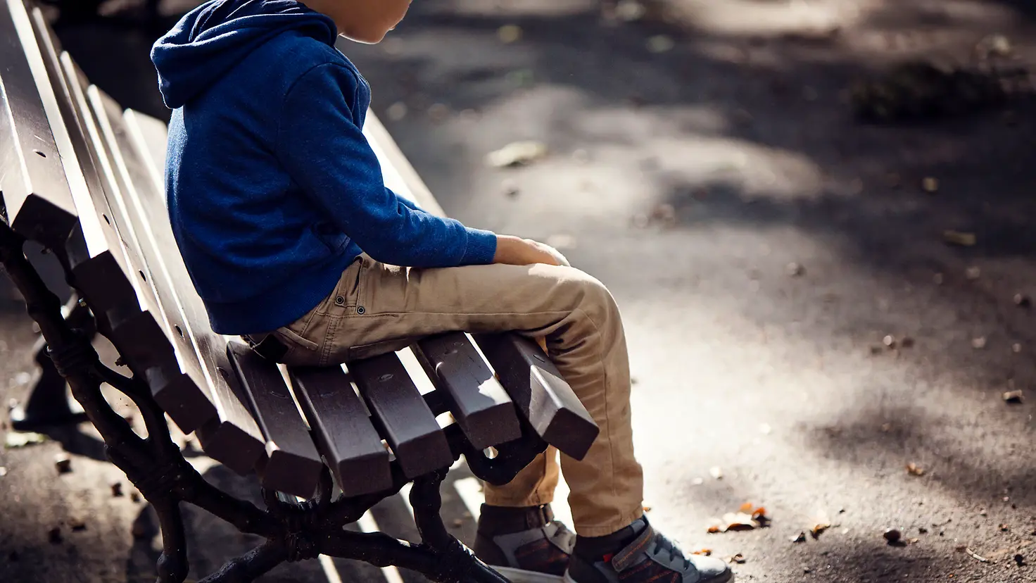 Kind sitzt alleine und verloren auf einer Parkbank