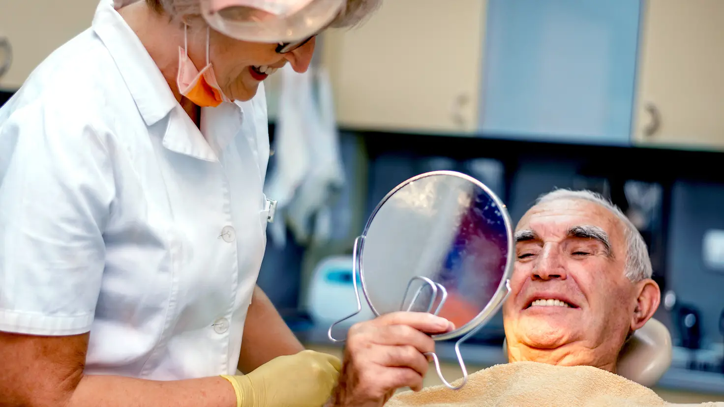 Ein ältere Mann beim Zahnarzt betrachtet seine Zähne im Handspiegel