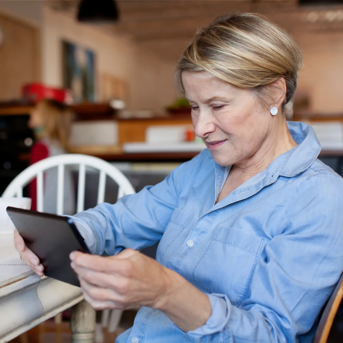 Eine ältere Frau sitzt mit Tablet am Küchentisch