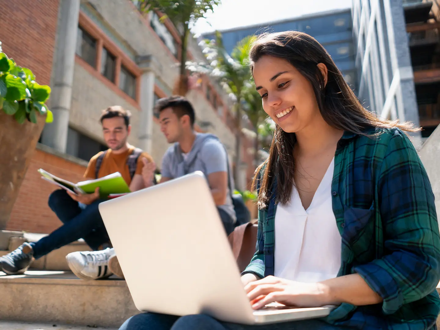 Eine Studentin sitzt mit Laptop vor einem Gebäude