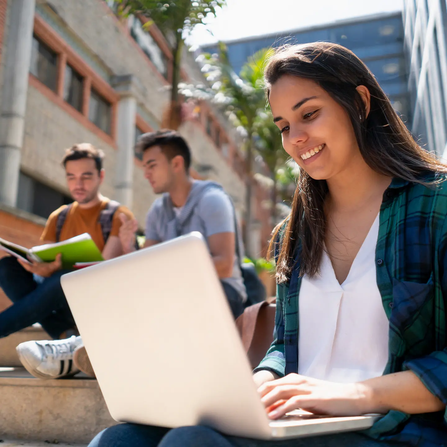 Eine Studentin sitzt mit Laptop vor einem Gebäude