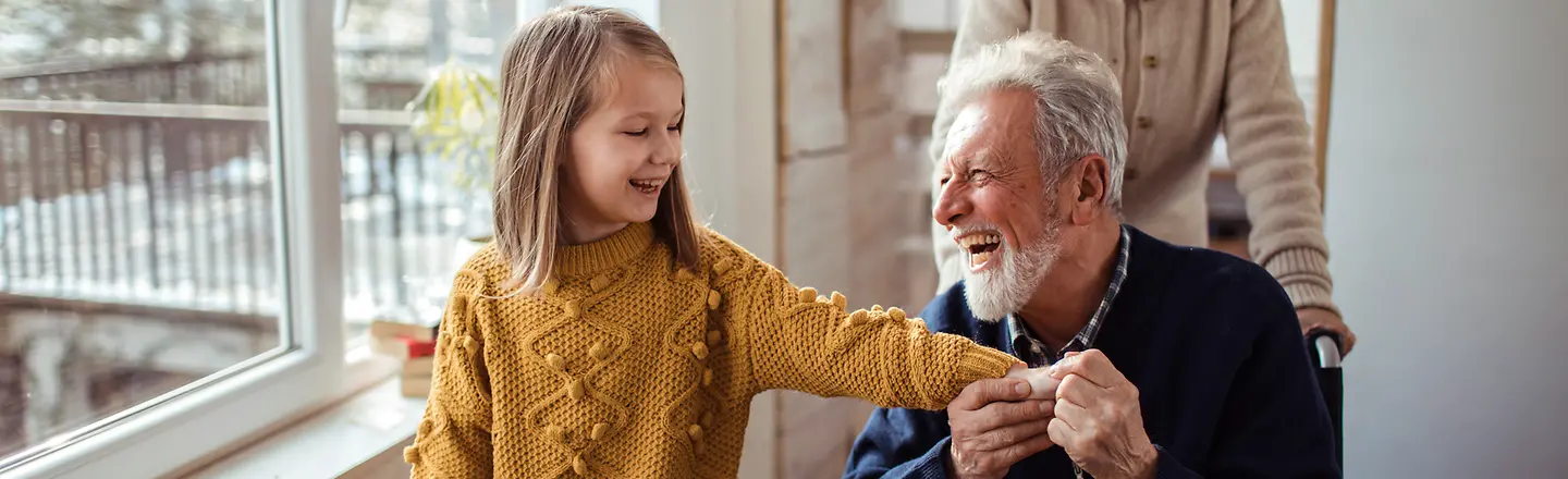 Ein älterer Mann im Rollstuhl wird von einer älteren Frau geschoben und hält die Hand seiner Enkelin