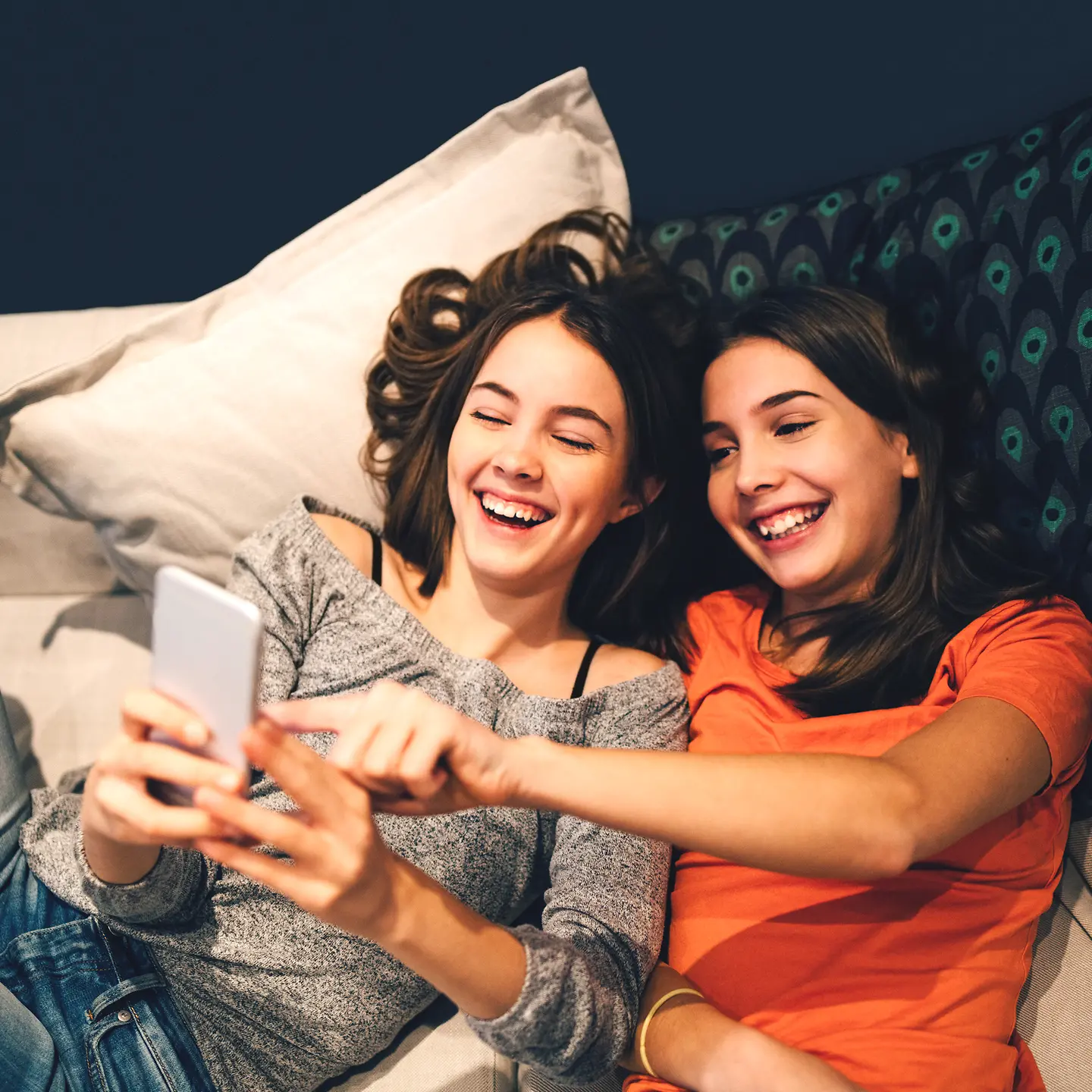 Zwei Jugendliche liegen auf dem Sofa und schauen auf ein Smartphone