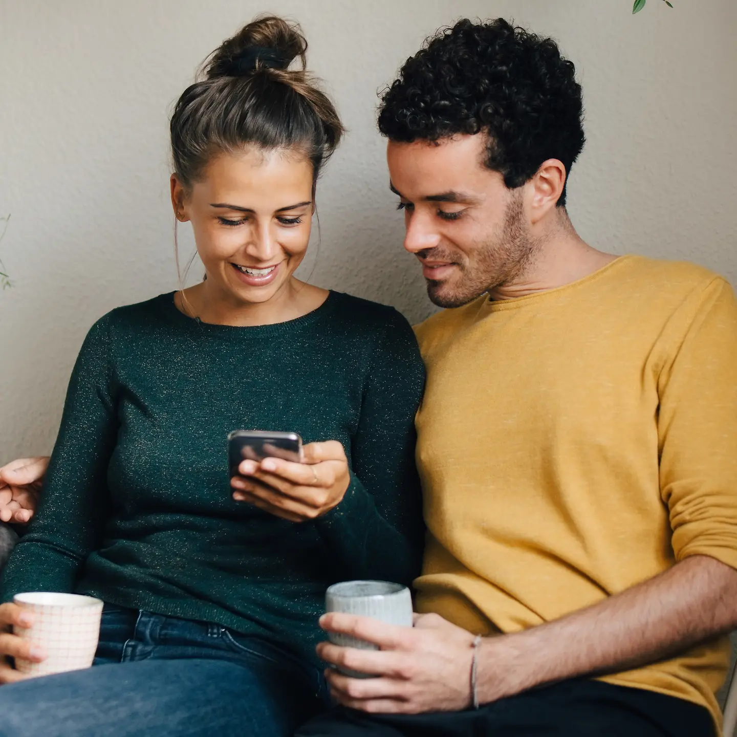 Ein junges Paar sitzt nah zusammen auf einer Bank und schaut auf ein Smartphone