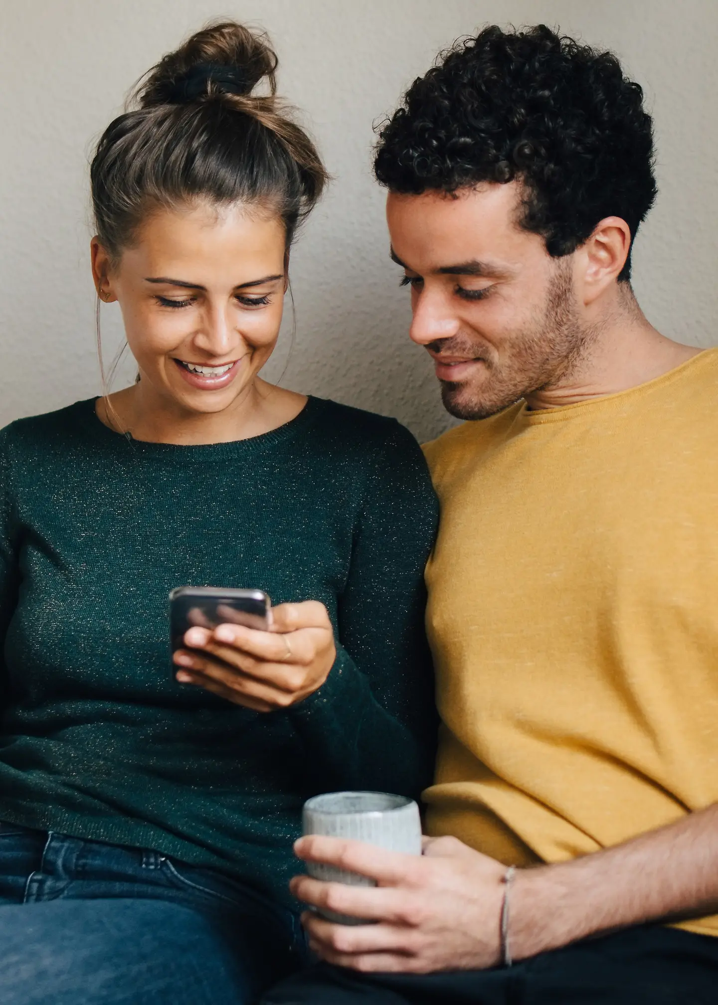 Ein junges Paar sitzt nah zusammen auf einer Bank und schaut auf ein Smartphone