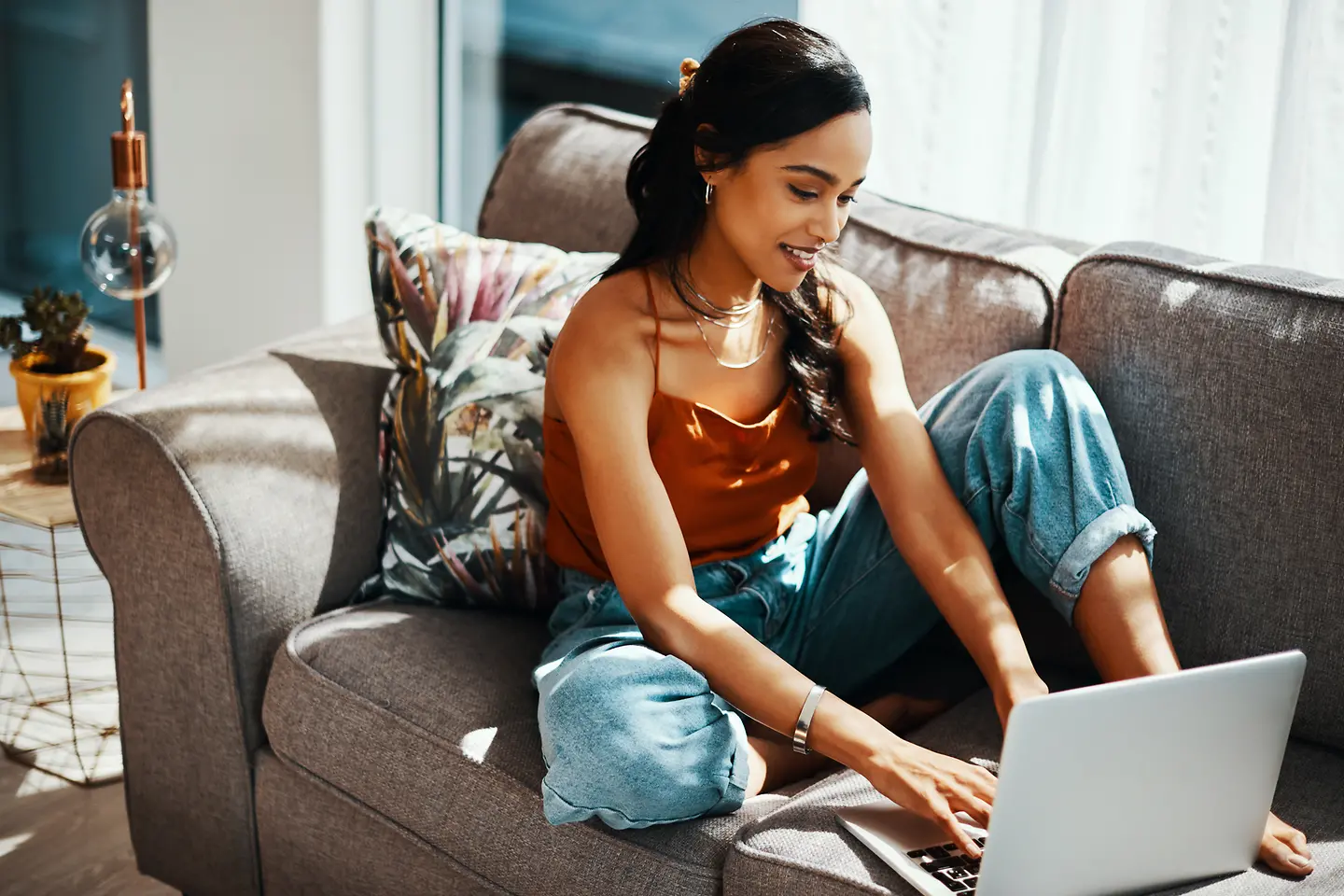 Eine junge Frau sitzt auf der Couch und arbeitet an einem Laptop