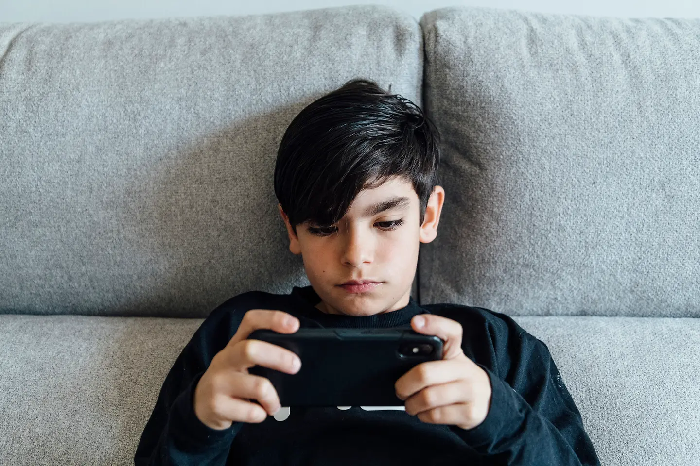 Ein Junge sitzt auf der Couch und schaut auf sein Smartphone