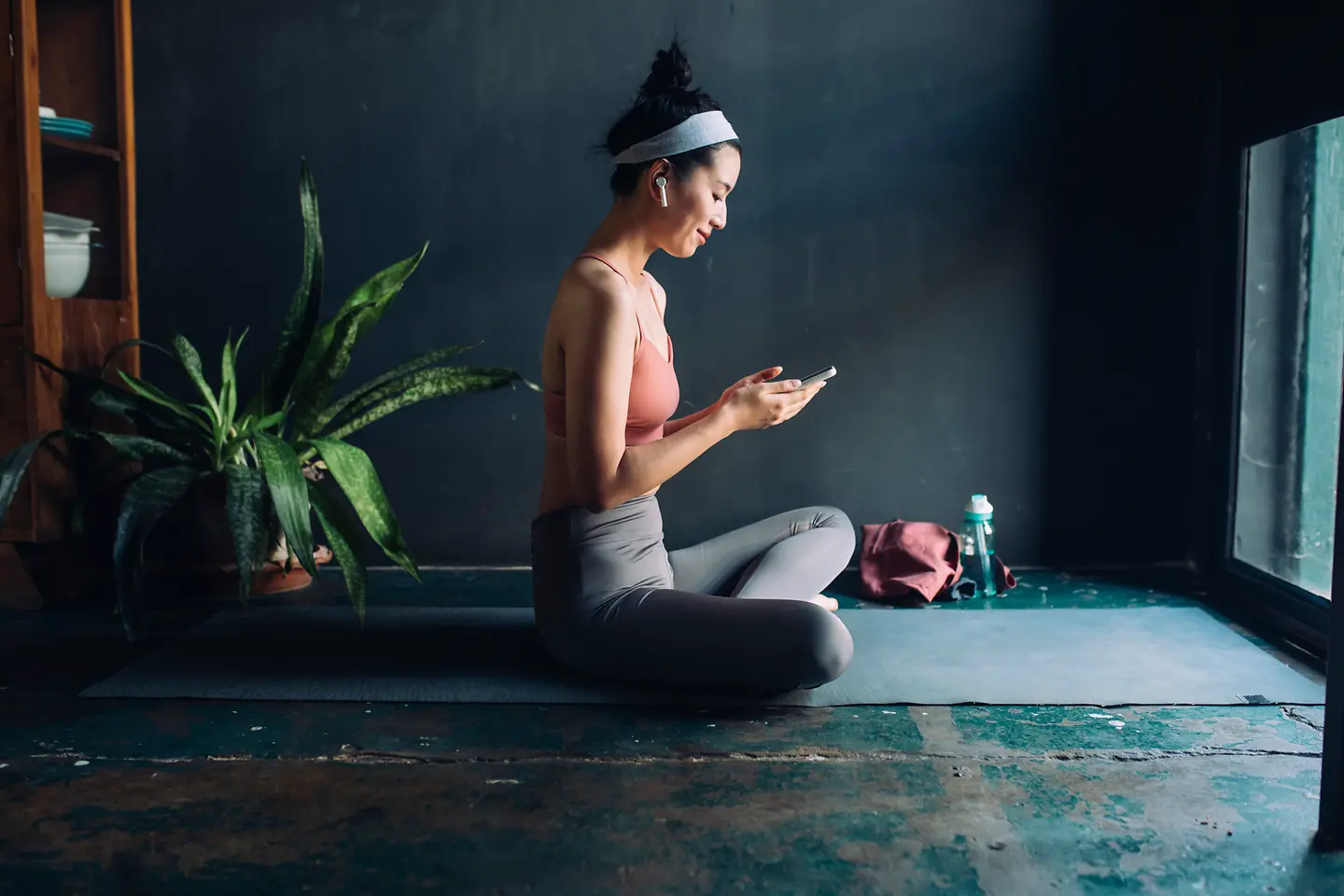 Eine junge Frau sitzt im Schneidersitz und schaut auf ein Smartphone