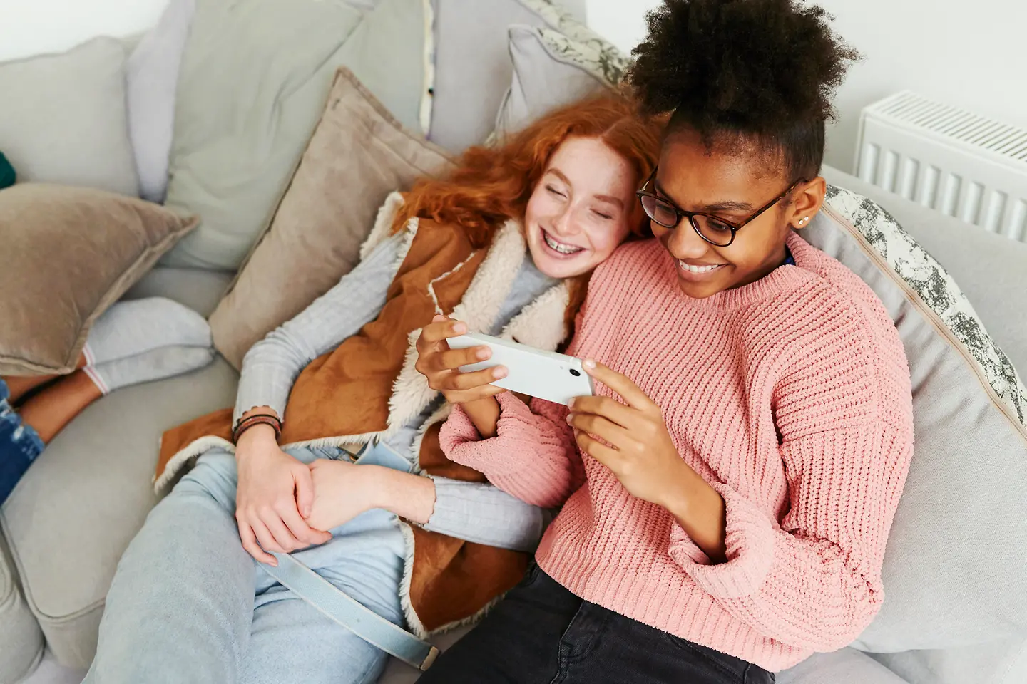 Zwei Mädchen sitzen auf einer Couch und schauen auf ein Smartphone