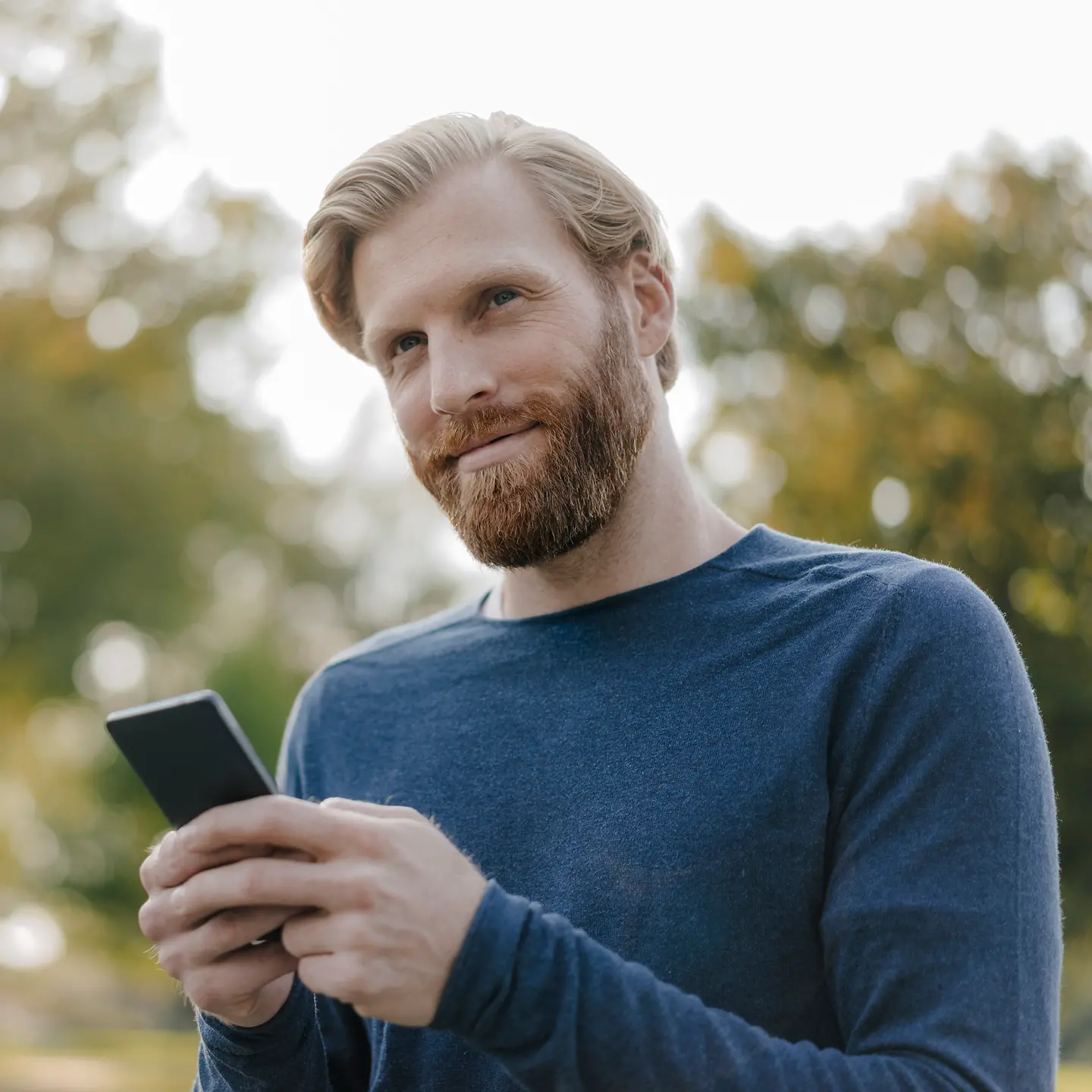 Junger Mann hält ein Smartphone in beiden Händen und schaut zufrieden