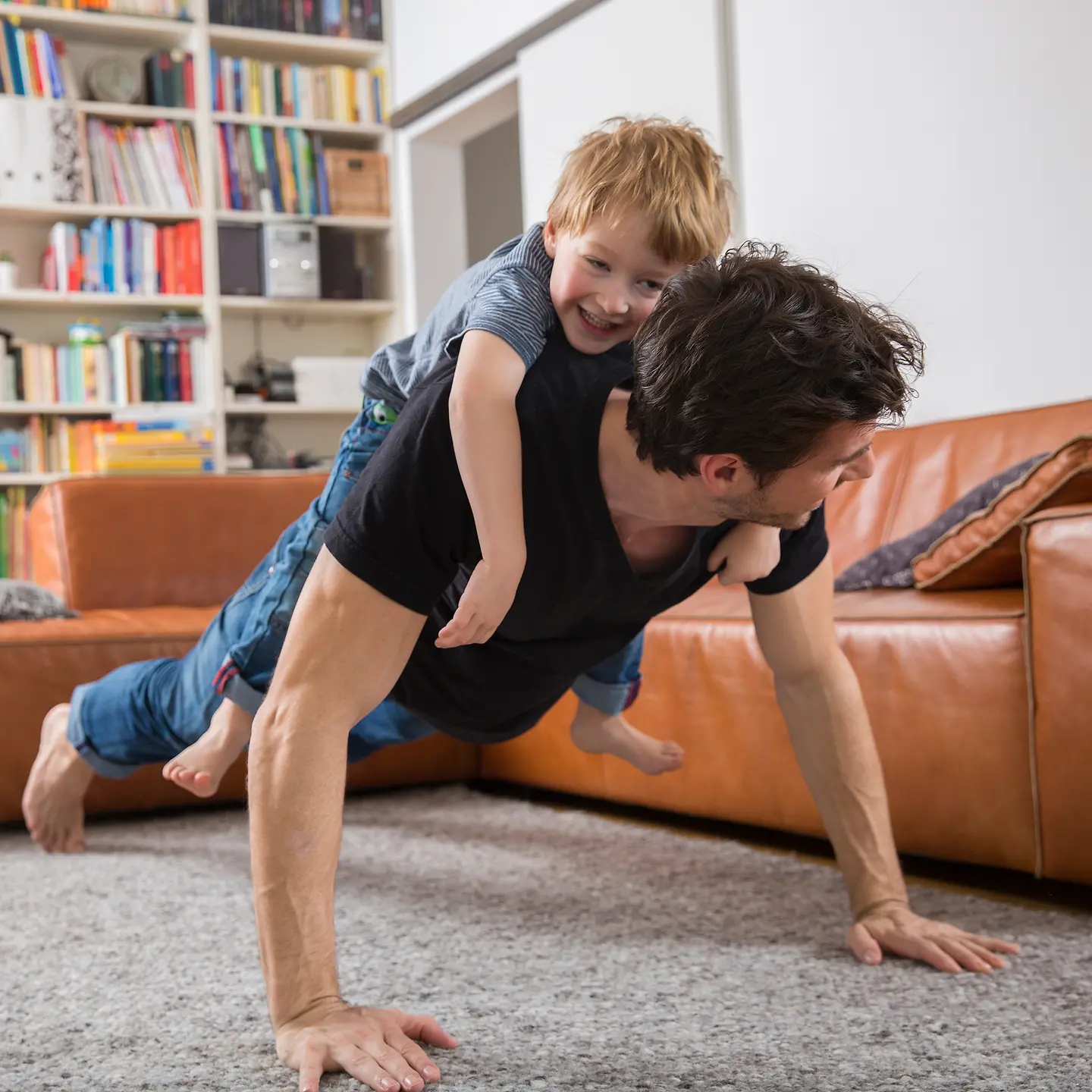 Ein Vater macht Liegestütze im Wohnzimmer mit seinem Sohn auf dem Rücken