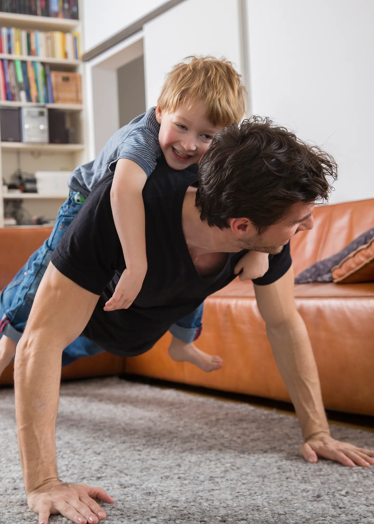 Ein Vater macht Liegestütze im Wohnzimmer mit seinem Sohn auf dem Rücken