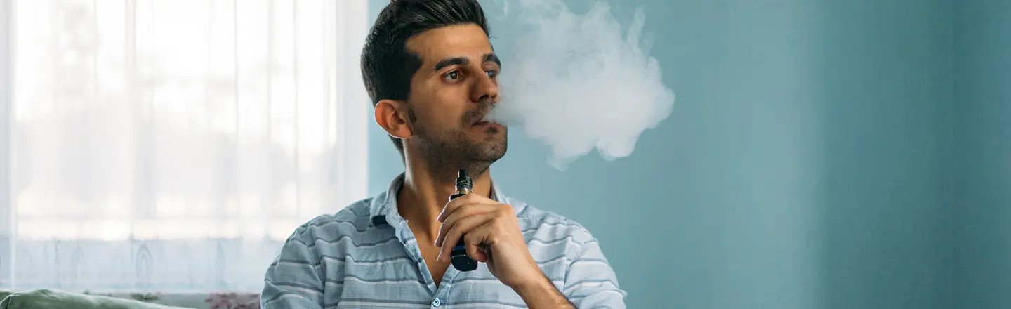 Ein Mann sitzt auf dem Sofa und raucht eine E-Zigarette.