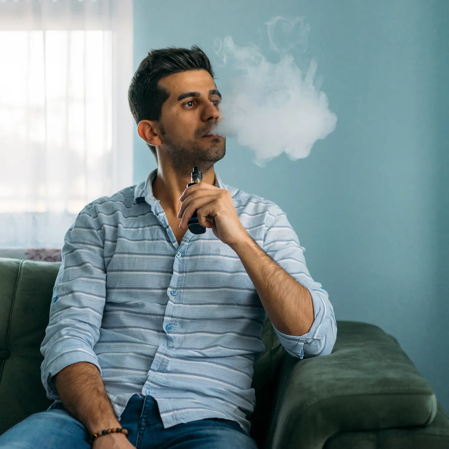 Ein Mann sitzt auf dem Sofa und raucht eine E-Zigarette.