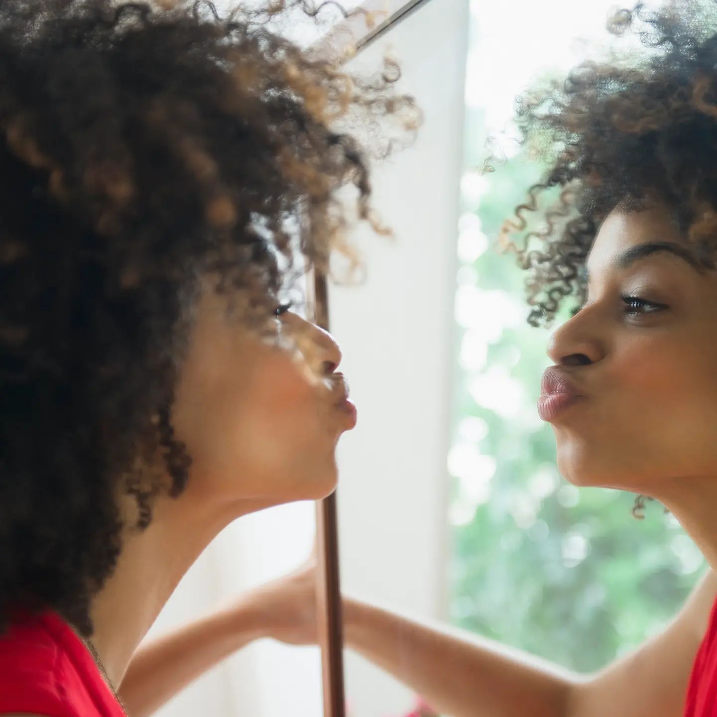 Eine junge Frau schaut in den Spiegel und macht einen Kussmund.