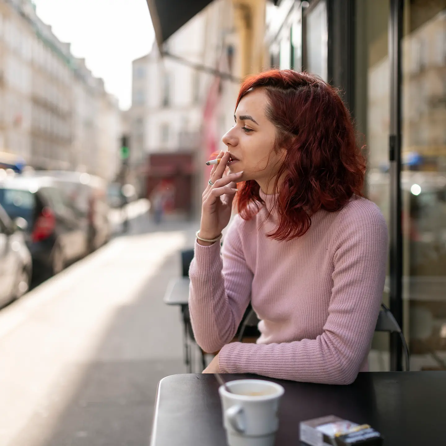 Eine junge Frau sitzt rauchend in einem Straßencafe.