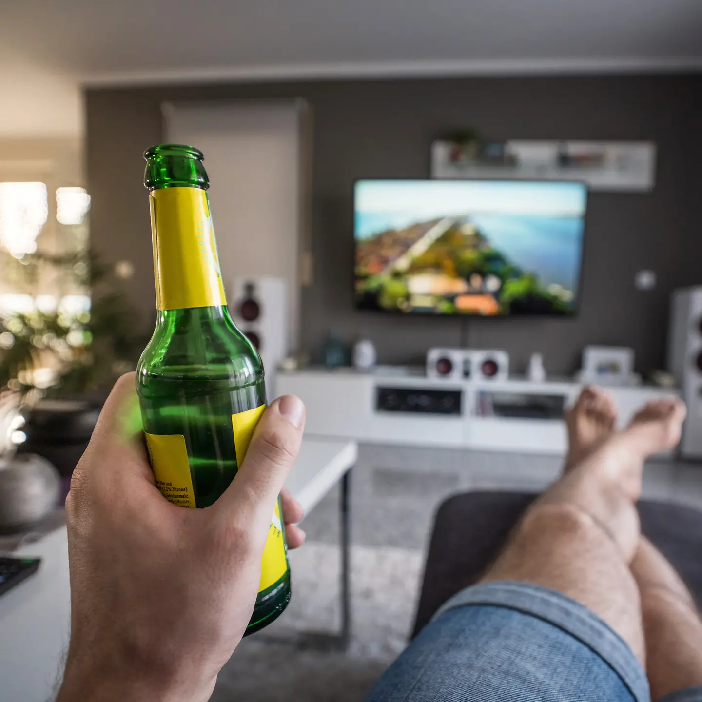 Mann sitzt im Wohnzimmer vor dem Fernseher mit Bierflasche in der Hand