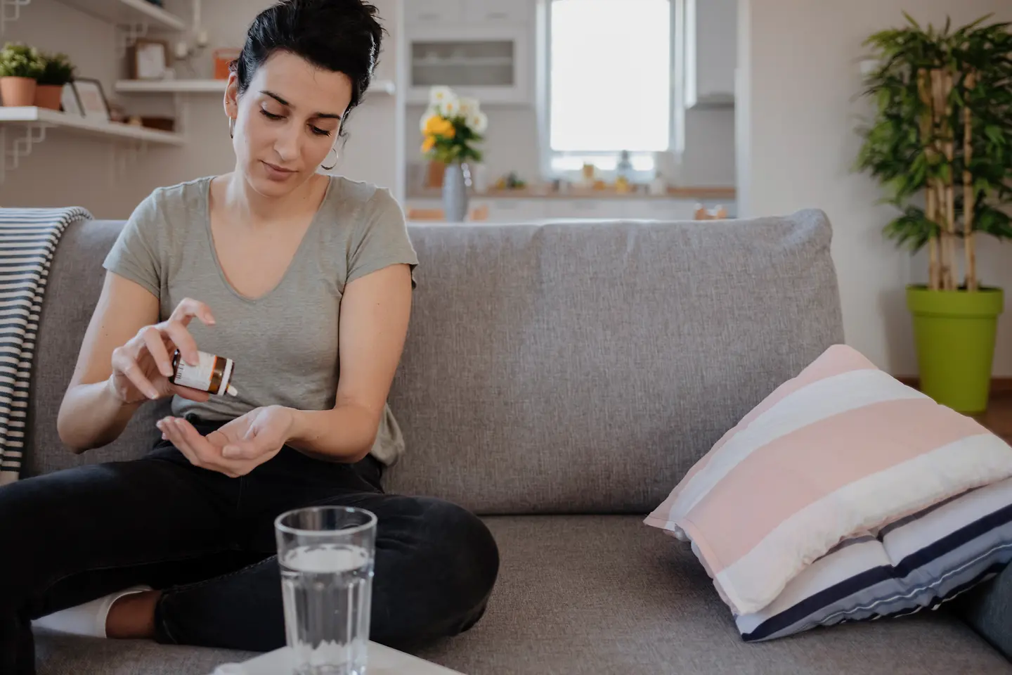 Eine junge Frau sitzt auf dem Sofa und hat Medikamente zu Einnehmen in der Hand