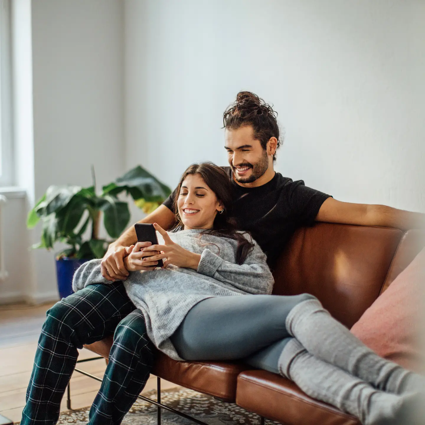 Ein junges Paar sitzt auf dem Sofa und schaut auf ein Smartphone