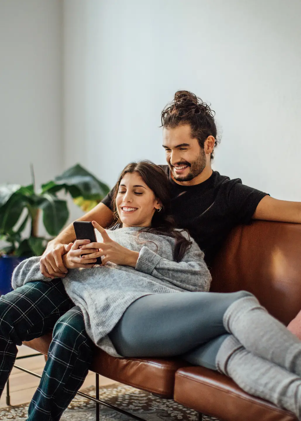 Ein junges Paar sitzt auf dem Sofa und schaut auf ein Smartphone
