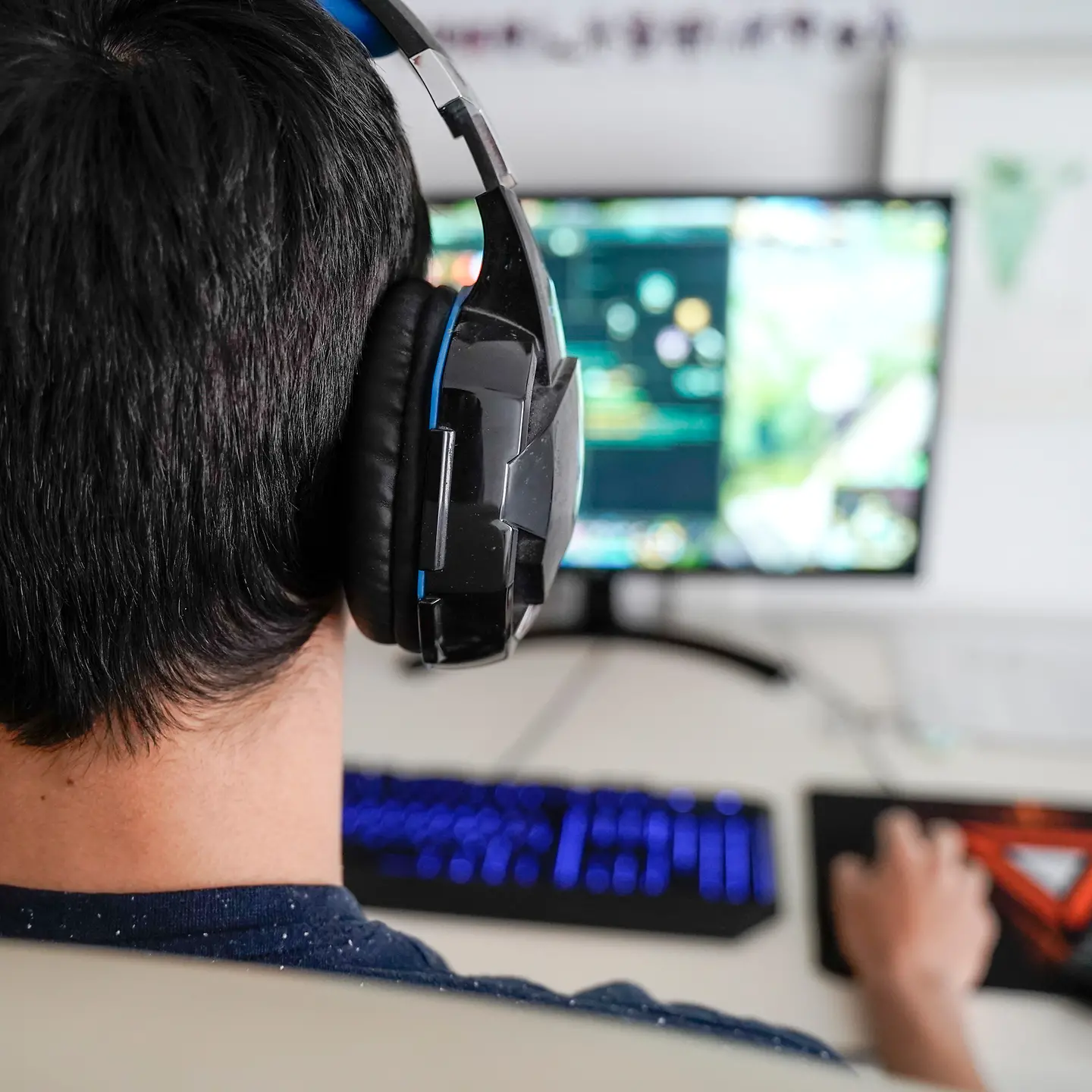 Ein junger Mann spielt ein Computerspiel an seinem PC und hat Kopfhörer auf.