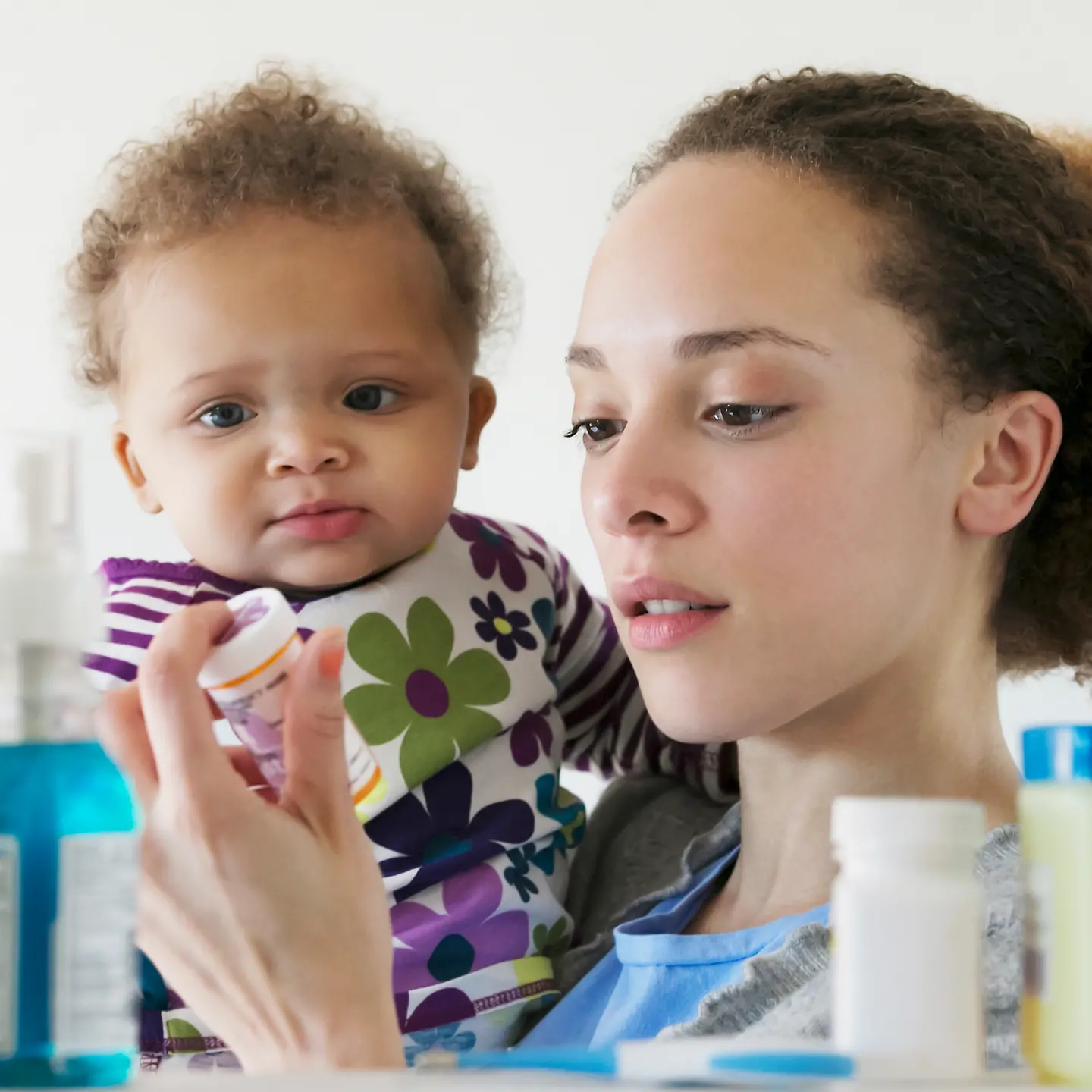 Eine Frau mit Kleinkind auf dem Arm schaut auf eine Medikamentenverpackung