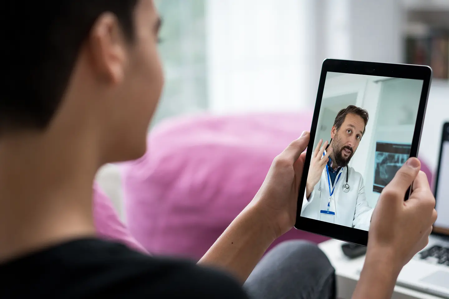 Ein Frau hält ein Tablet in der Hand, auf dem ein Arzt zu sehen ist.