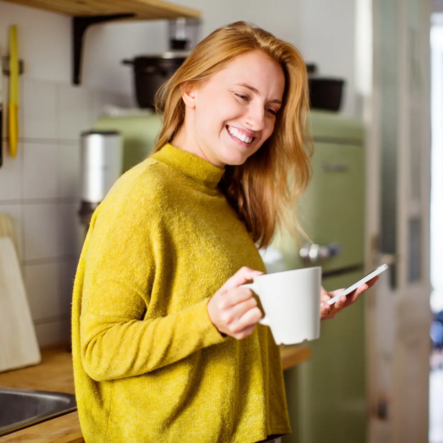 Frau steht in der Küche mit Kaffee und Mobiltelefon