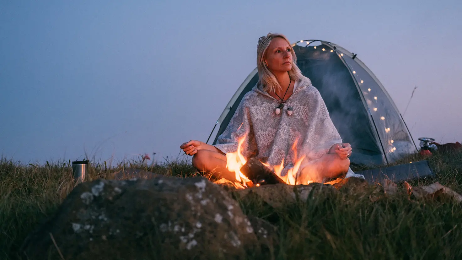 Junge Frau meditiert an einem Lagerfeuer