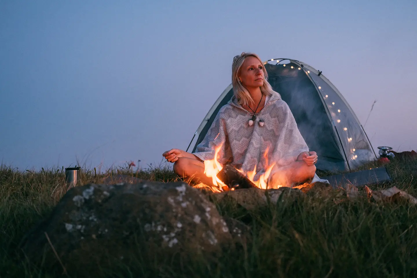 Junge Frau meditiert an einem Lagerfeuer