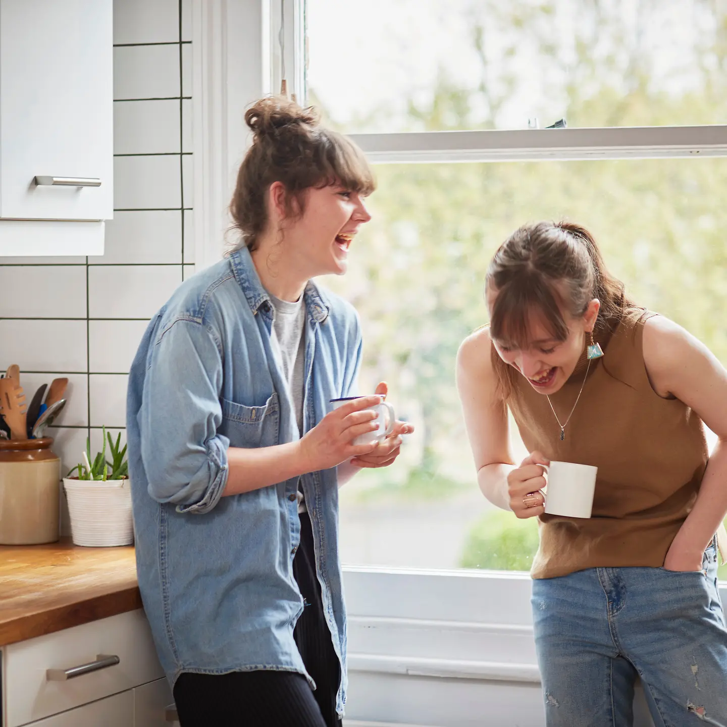 Zwei junge Frauen stehen in einer Küche und lachen sich kaputt