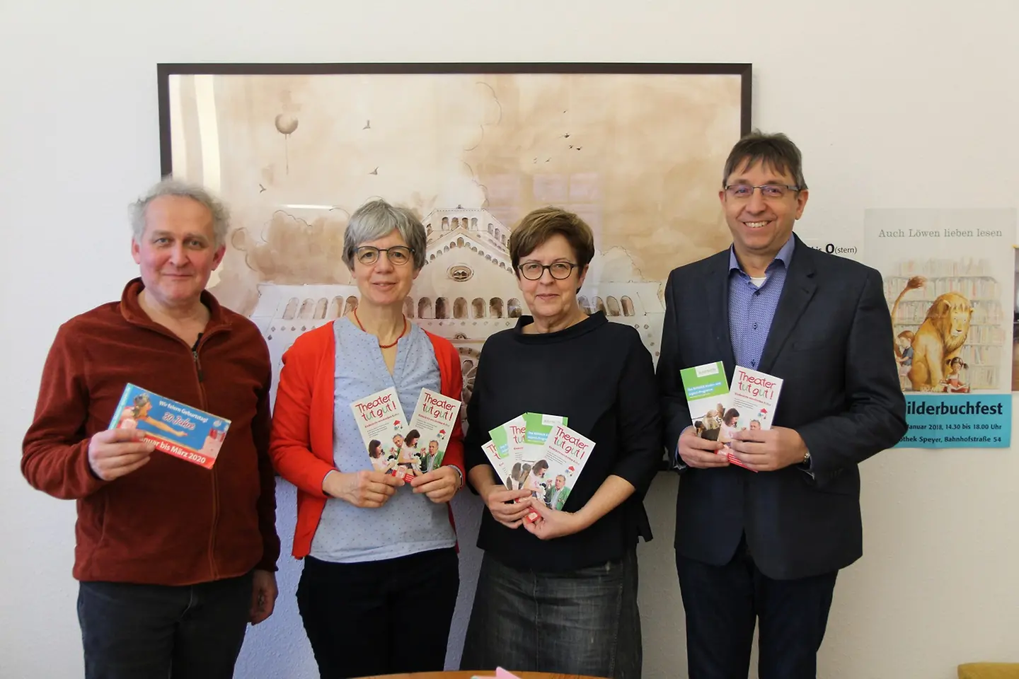 Die Partner der Aktion Theater tut gut stehen vor einer Wand und halten Flyer in der Hand