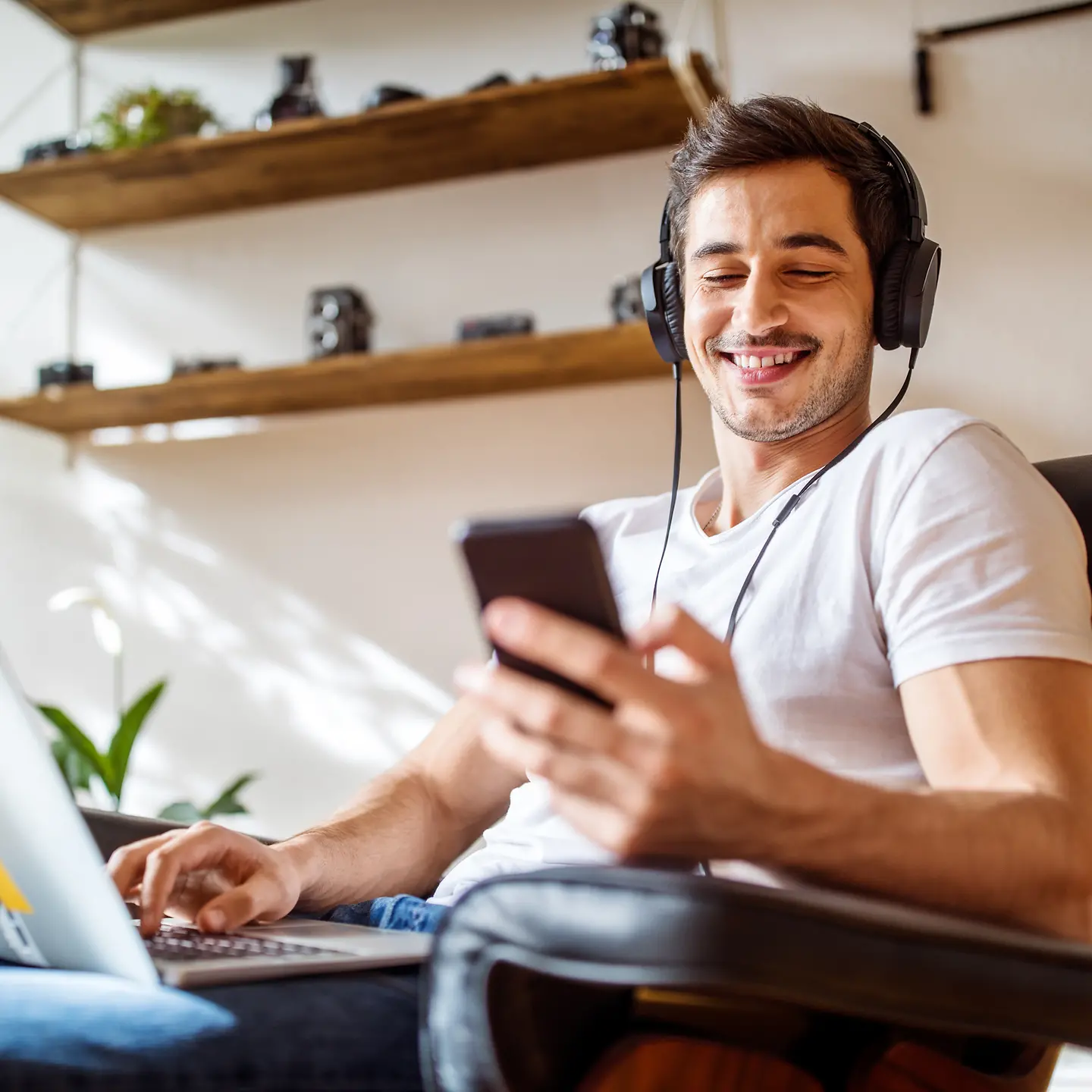 Ein Mann hat Kopfhörer auf und einen Laptop auf seinem Schoß.