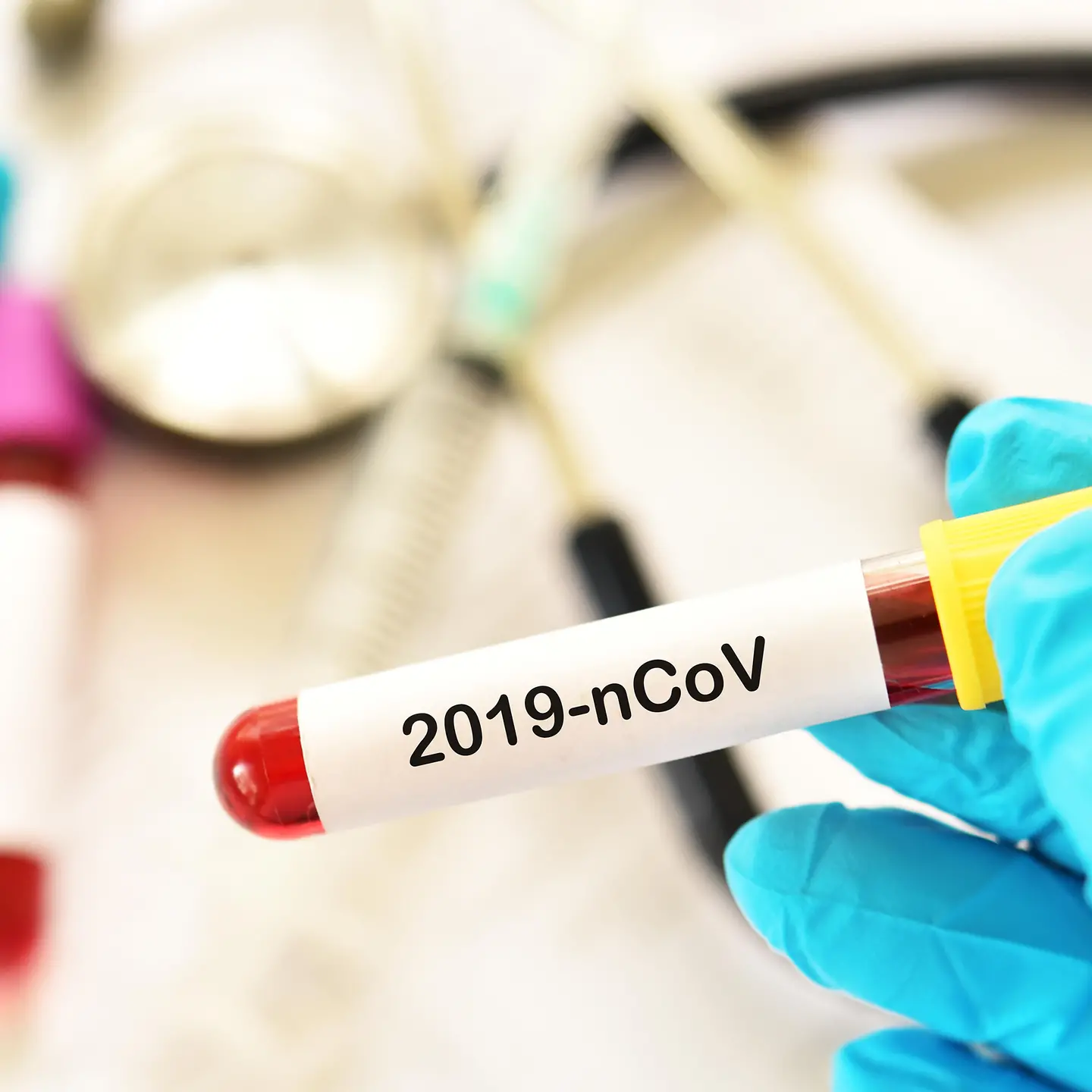 Eine Hand mit blauem Schutzhandschuh hält ein Reagenzglas mit der Aufschrift 2019-n-Cov