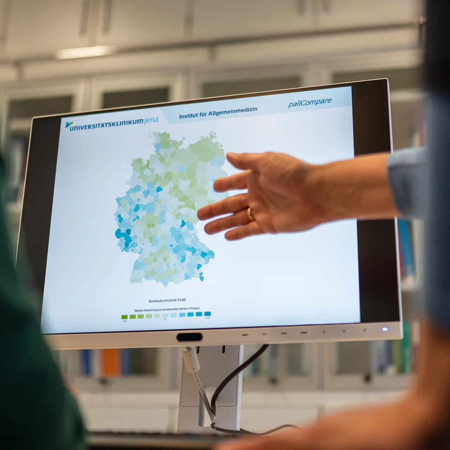 Eine Person zeigt mit einer Hand auf einen Infografik auf einem Bildschirm.