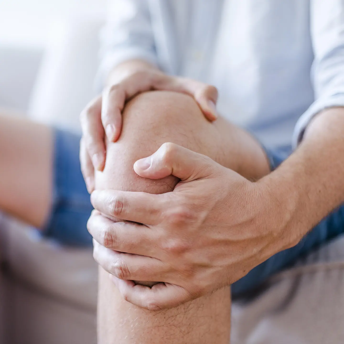 Ein Mann sitzt auf einem Sofa und umfasst sich vor Schmerzen das Knie.