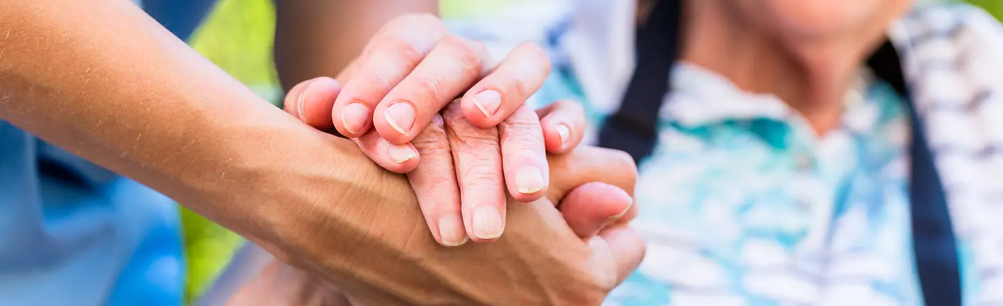 Eine Pflegekraft hält einer alten Person die Hand