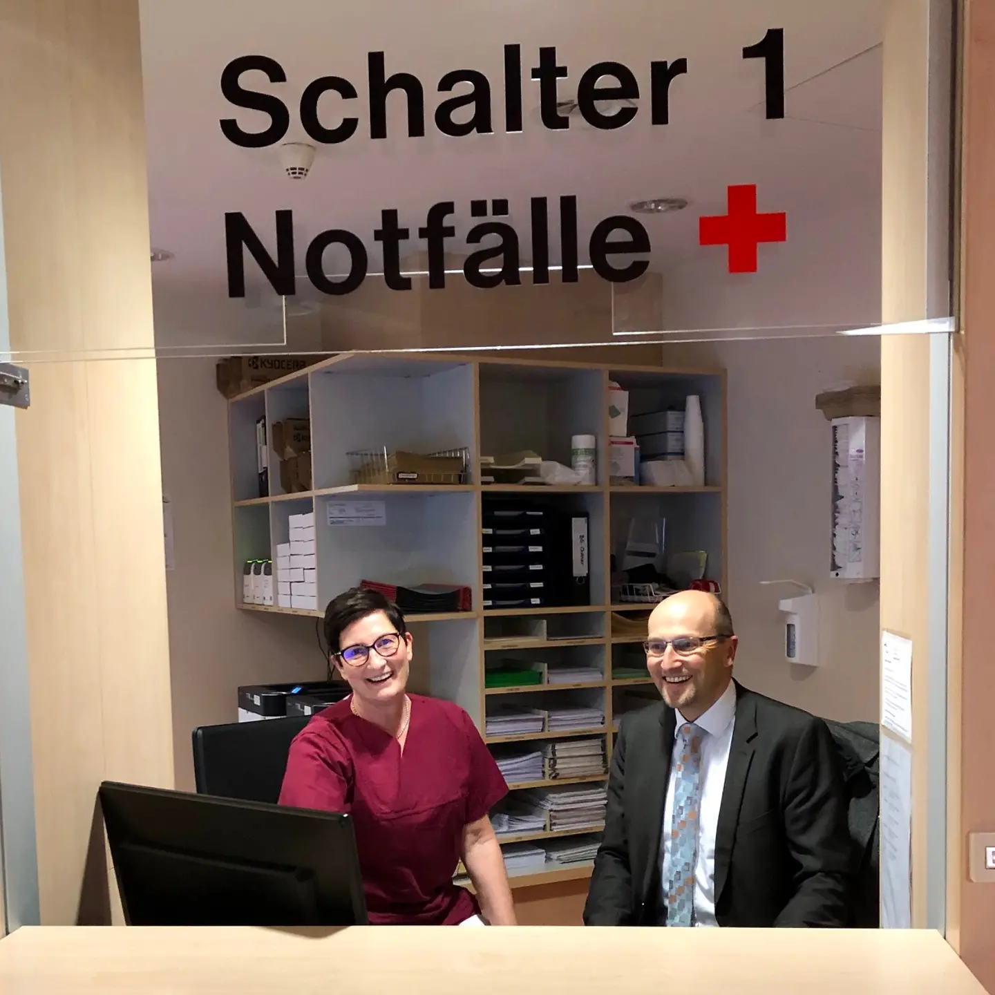 Eine Ärztin und Winfried Plötze sitzen für ein Foto gemeinsam am Schalter für Notfälle in einem Krankenhaus.