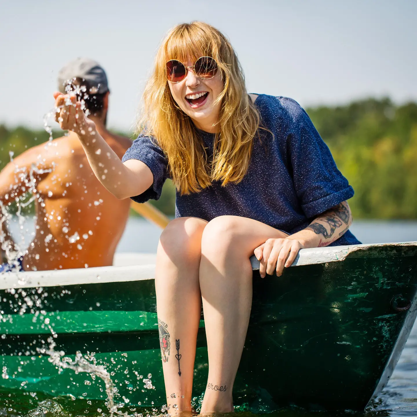 Une jeune femme est assise dans un bateau, rit et éclabousse de l'eau.